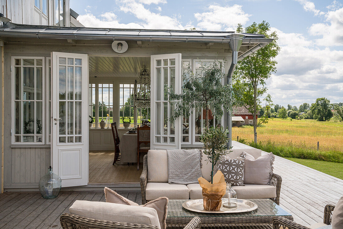 Blick von der Terrasse mit Rattanmöbeln in den Wintergarten