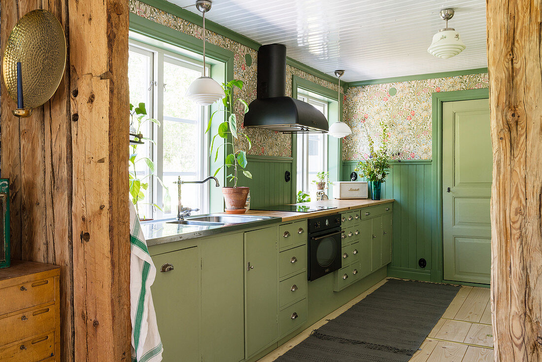 Green base units and nostalgic wallpaper in the kitchen