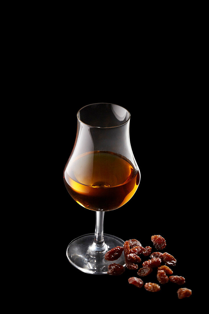 A glass of rum with a pile of raisins