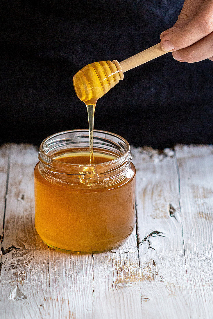 Honig fließt von Honiglöffel in Honigglas