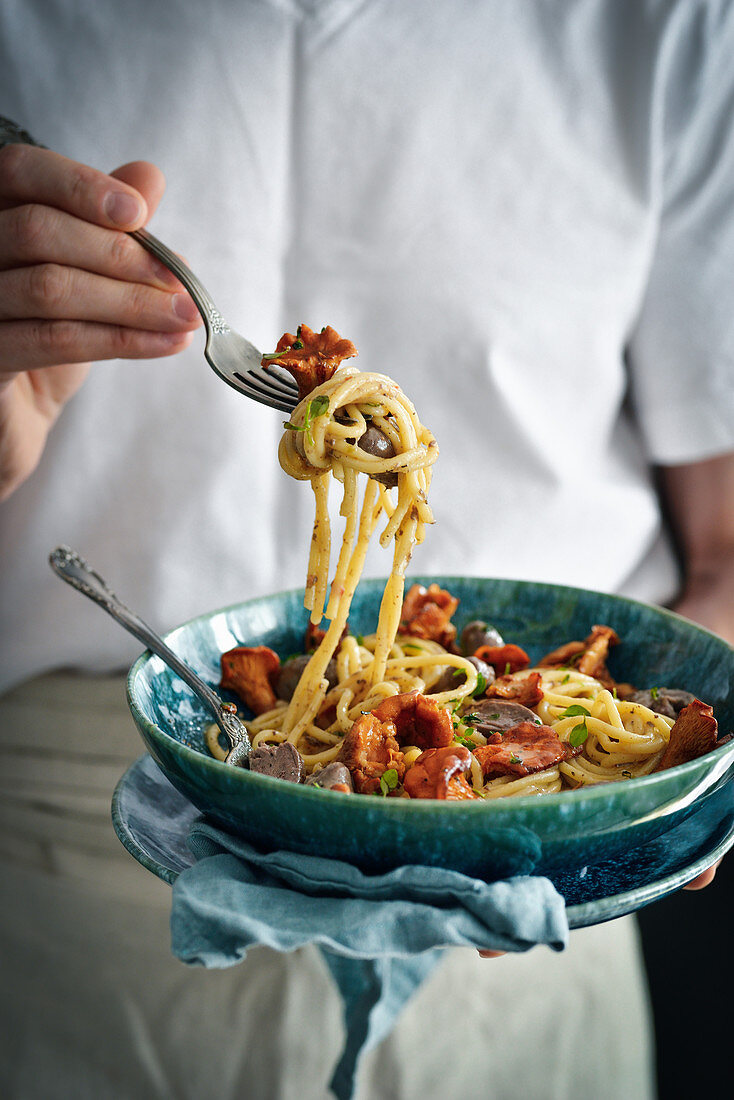 The man is holding a plate of pasta and mushrooms