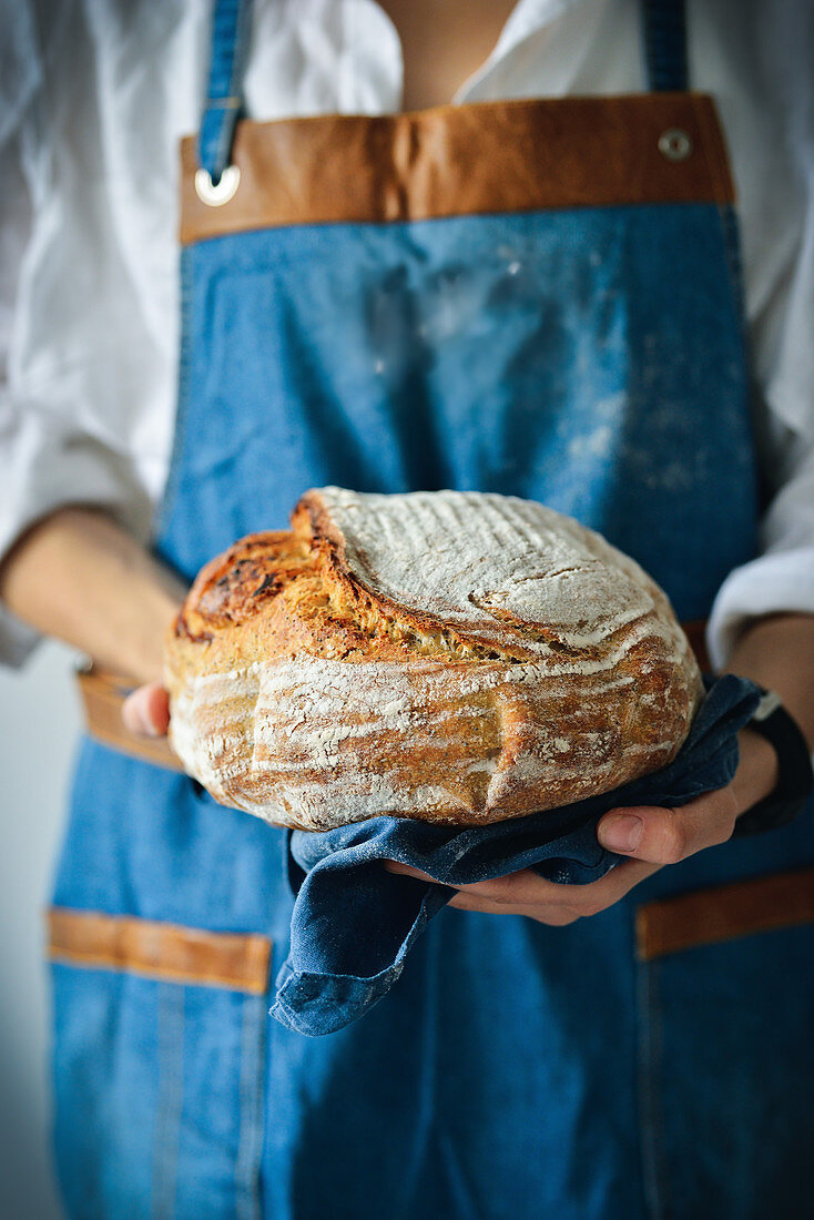 Woman is holding a large sourdough bread
