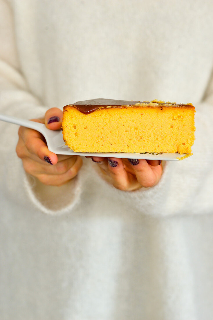 Woman is holding a plate with a piece of pumpkin cheesecake