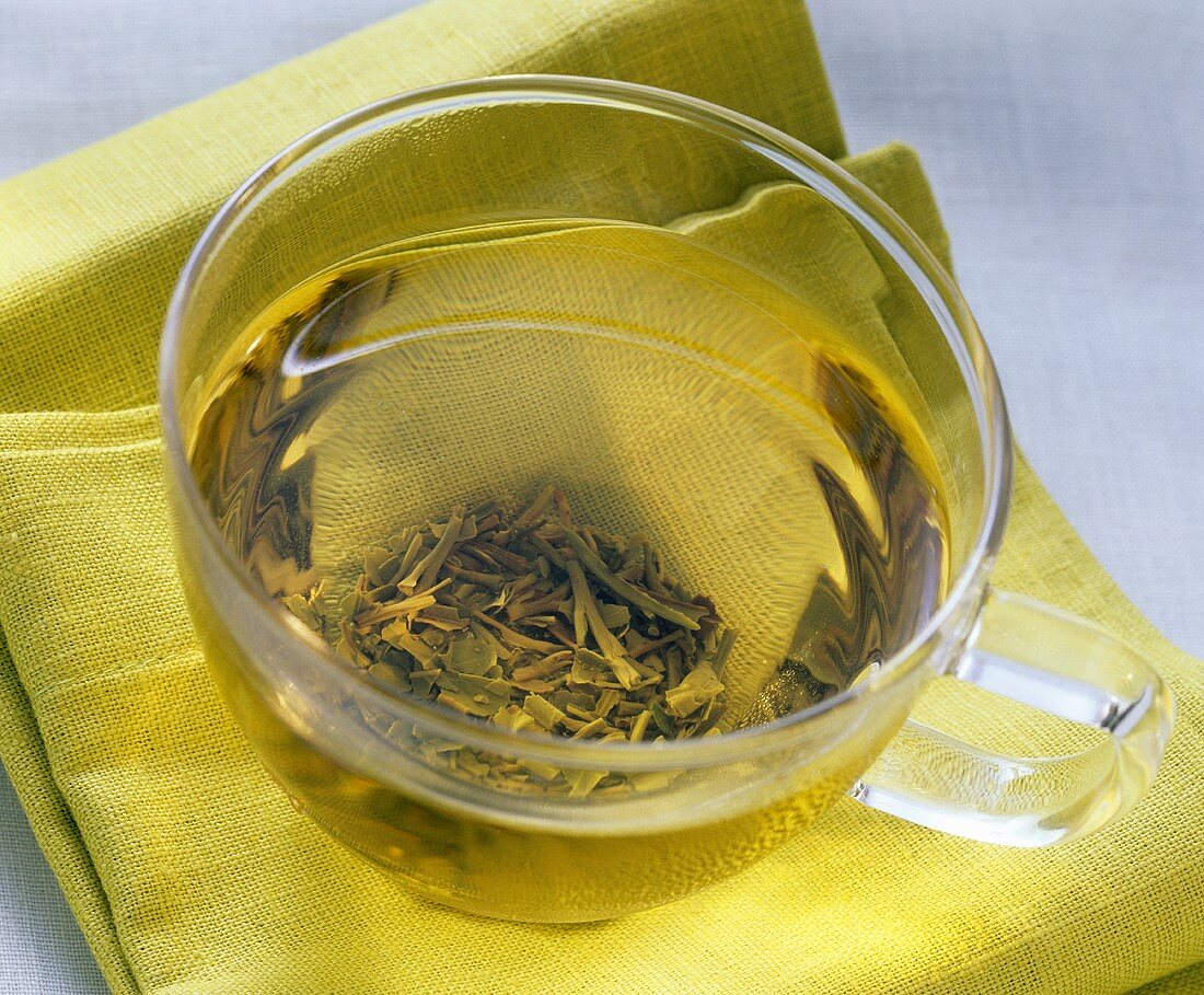 Grüner Darjeeling Tee in Glastasse auf hellgrünem Tuch