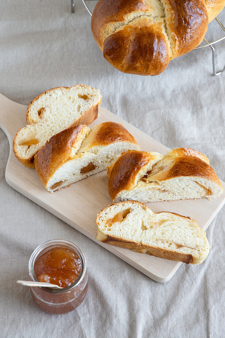 Fresh brioche made from butter dough with jam on wooden board next to glass jar of jam