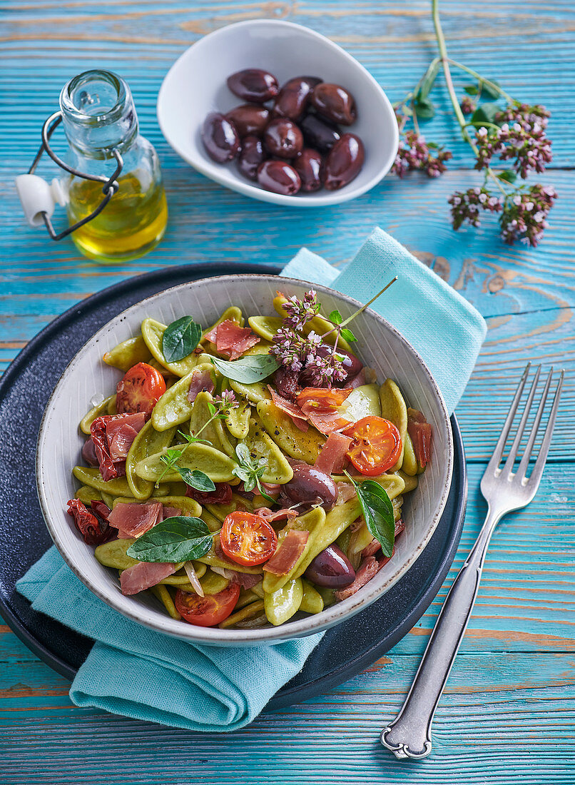 Spinach pasta leaves with tomatoes, dried ham and olives