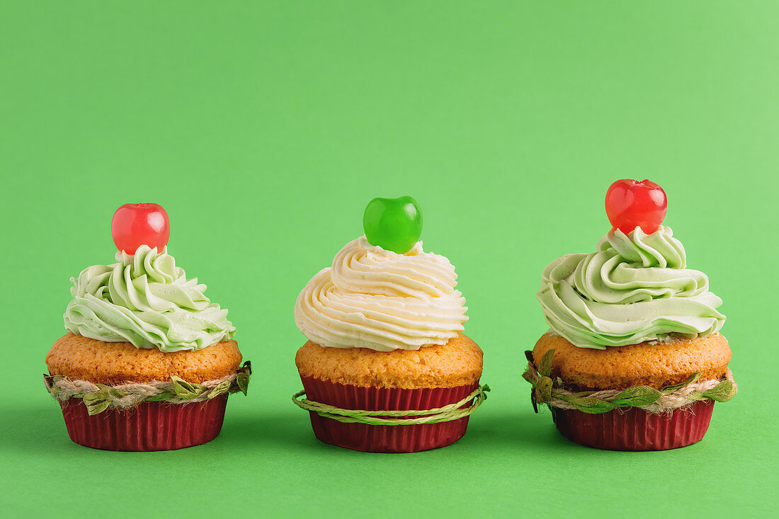 Festive Christmas cupcakes with cherry on green background
