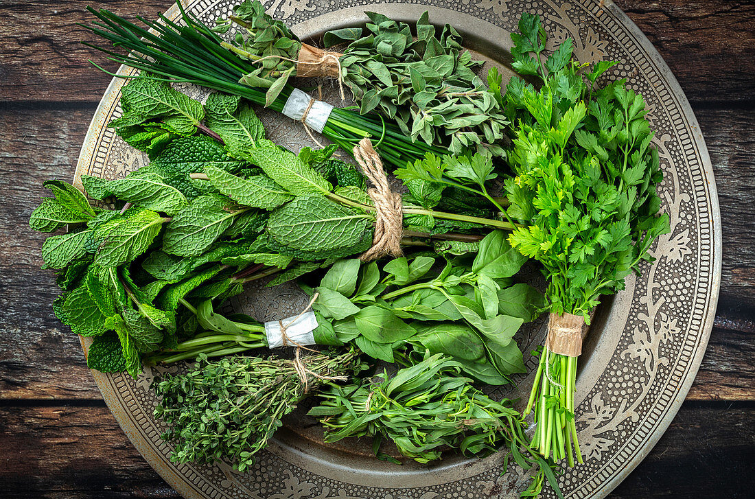 Round plate filled with various fresh green aromatic herbs placed on wooden table