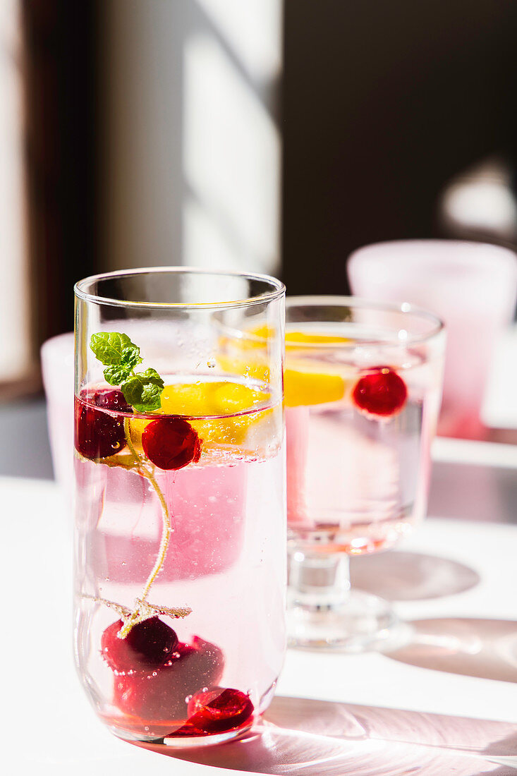 Fresh detox water with cherry and mint placed on table lit by sun in modern apartment