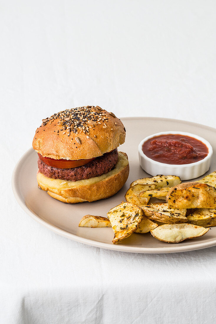 Hamburger with meat cutlet and golden buns decorated with mix of sesame seeds near crunchy toasted potato slices with spices and salsa barbecue on ceramic plate