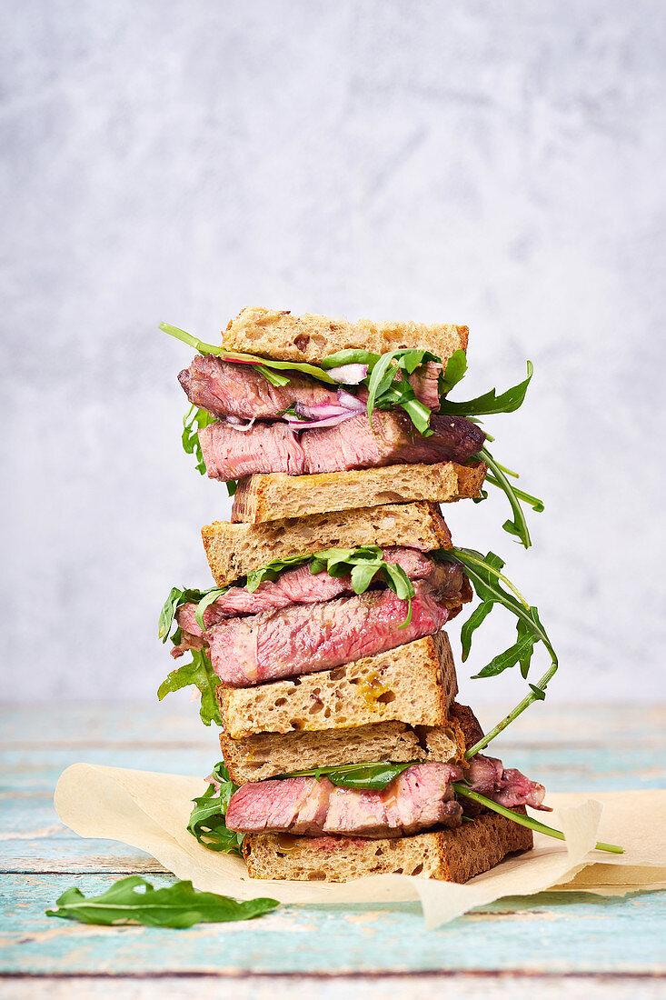 A pile of beef steak sandwich with arugula and mustard dressing against bright background