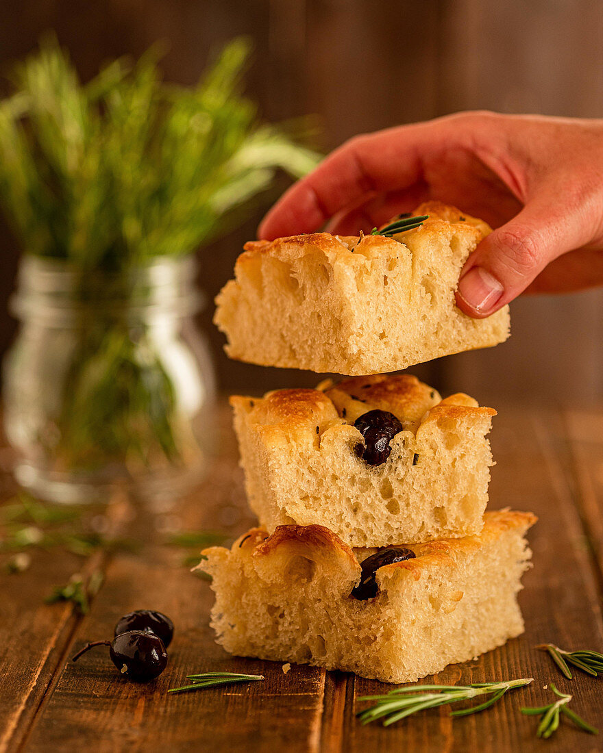 Taking piece of fresh homemade focaccia bread with olives and rosemary