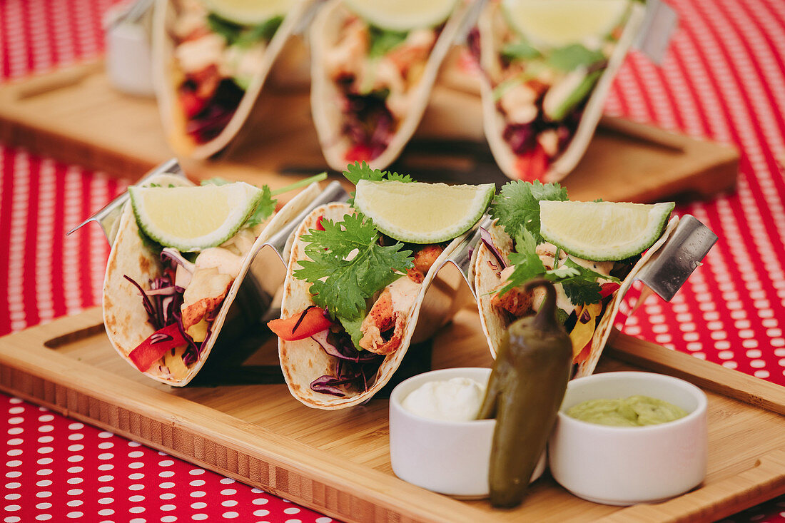 Traditional Mexican tacos served on wooden tray on table with various food