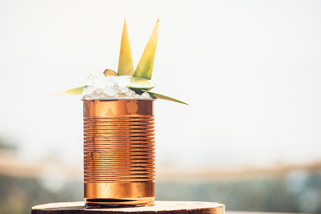 Cold drink with lime and ice served in metal can garnished with fresh green leaves