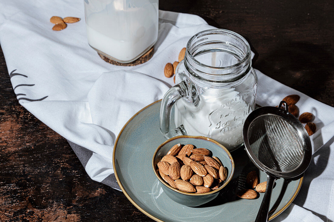 Bowl of natural almonds placed near glass jar of fresh vegan milk on plate and napkin in dark room