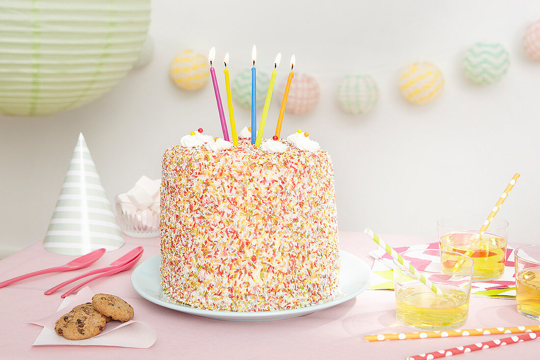 A birthday cake covered in sprinkles with five candles