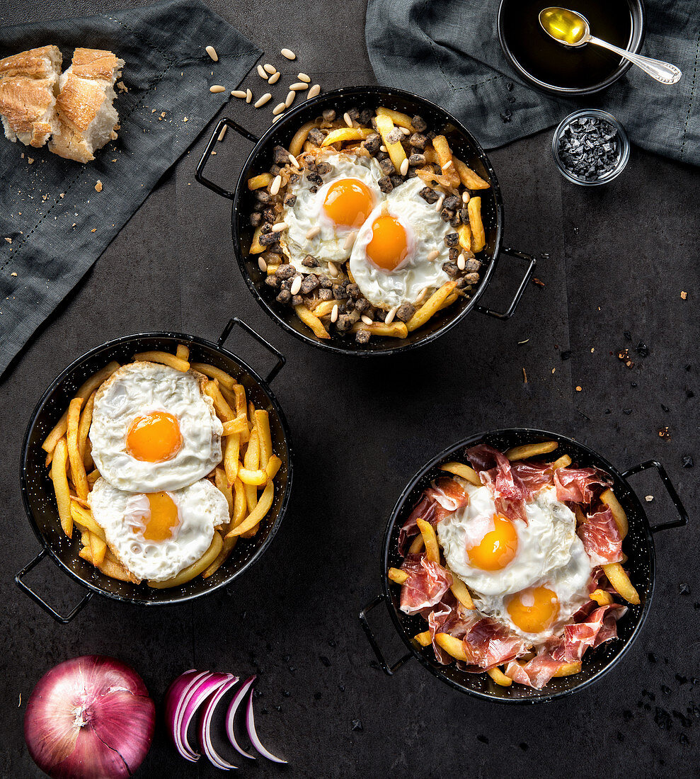 Fried potato and eggs in black round pans with adding roasted ham or black pudding in composition with bread and ingredients