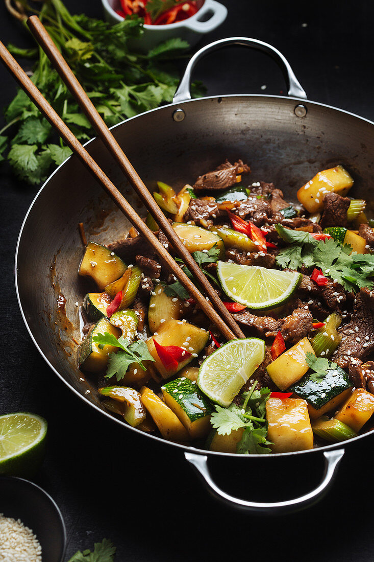 Asian spicy wok stir fried dish with meat and zucchini garnished with fresh lime and cilantro