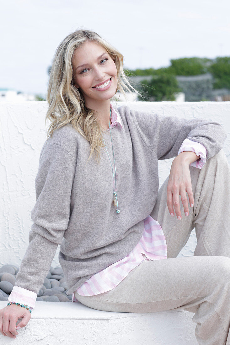 A young blonde woman on the beach wearing a light jumper and trousers