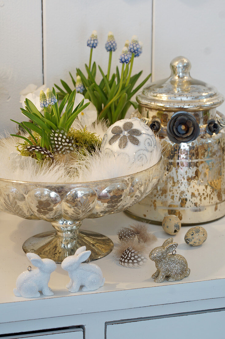 Grape hyacinth with glass egg in a pedestal bowl with feathers