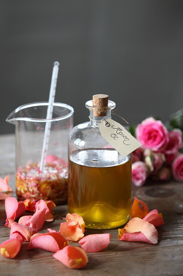 Rosenöl in Glasflasche daneben Rosenblütenblätter