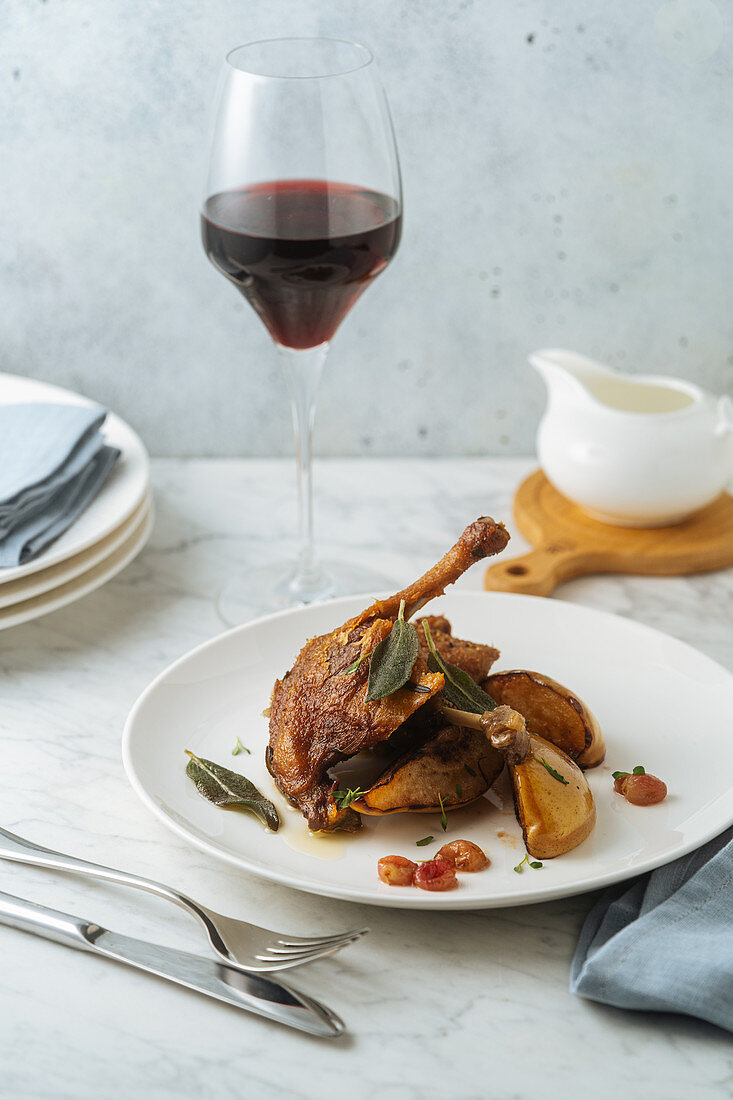Roasted quail garnished with pears and leaves served with glass of red wine
