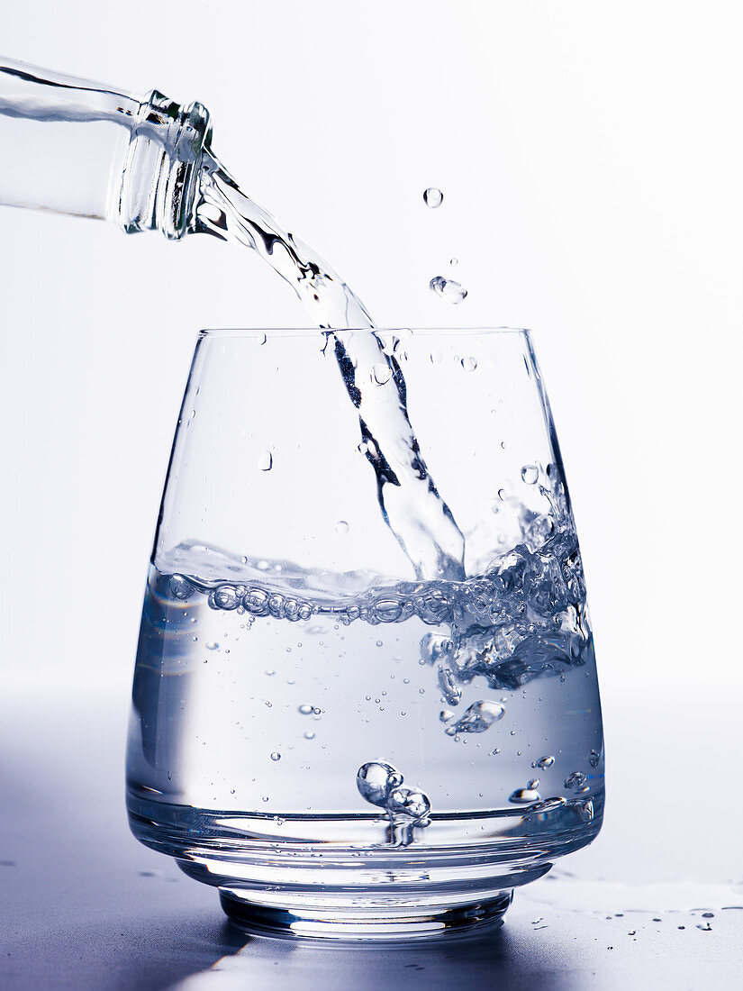Wasser aus Glasflasche in Glas gießen