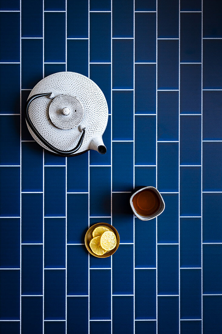 Teekanne und Teebecher auf blauem Fliesenuntergrund