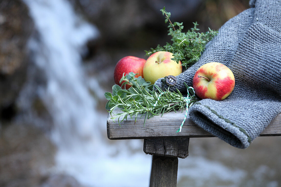 Apples and herbs on a wooden bench in front of a waterfall