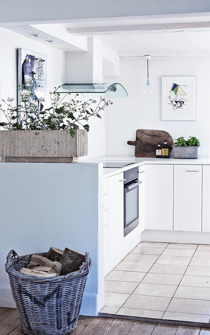 L-shaped, white fitted kitchen with basket of firewood in the foreground