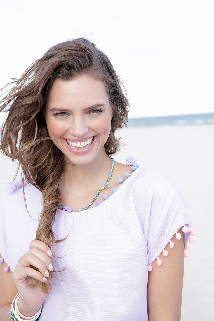 A young brunette woman by the sea wearing a pastel purple top