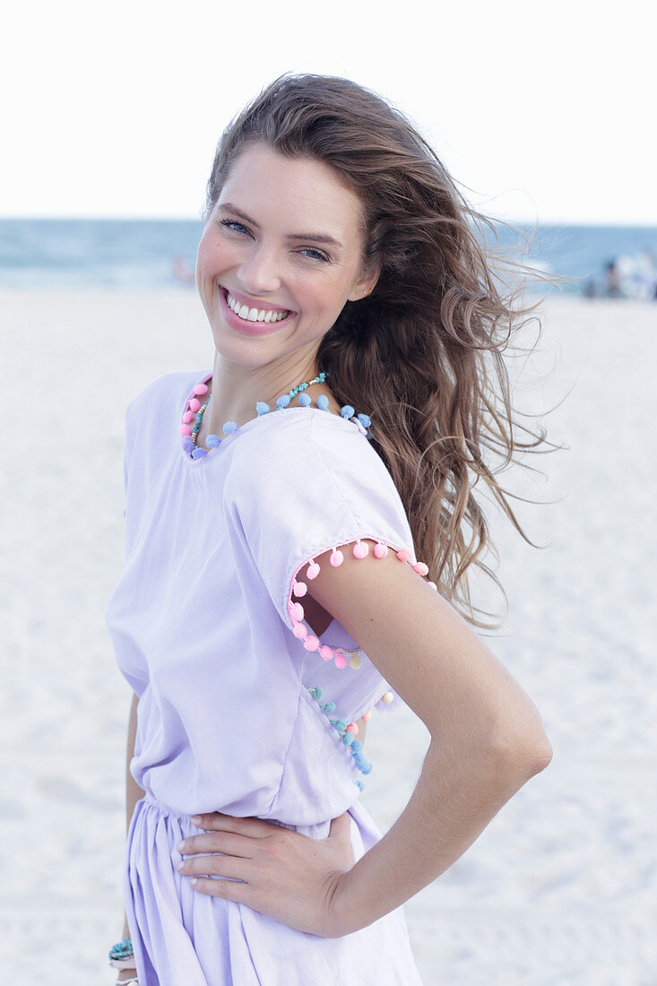 A young brunette woman by the sea wearing a pastel purple summer dress