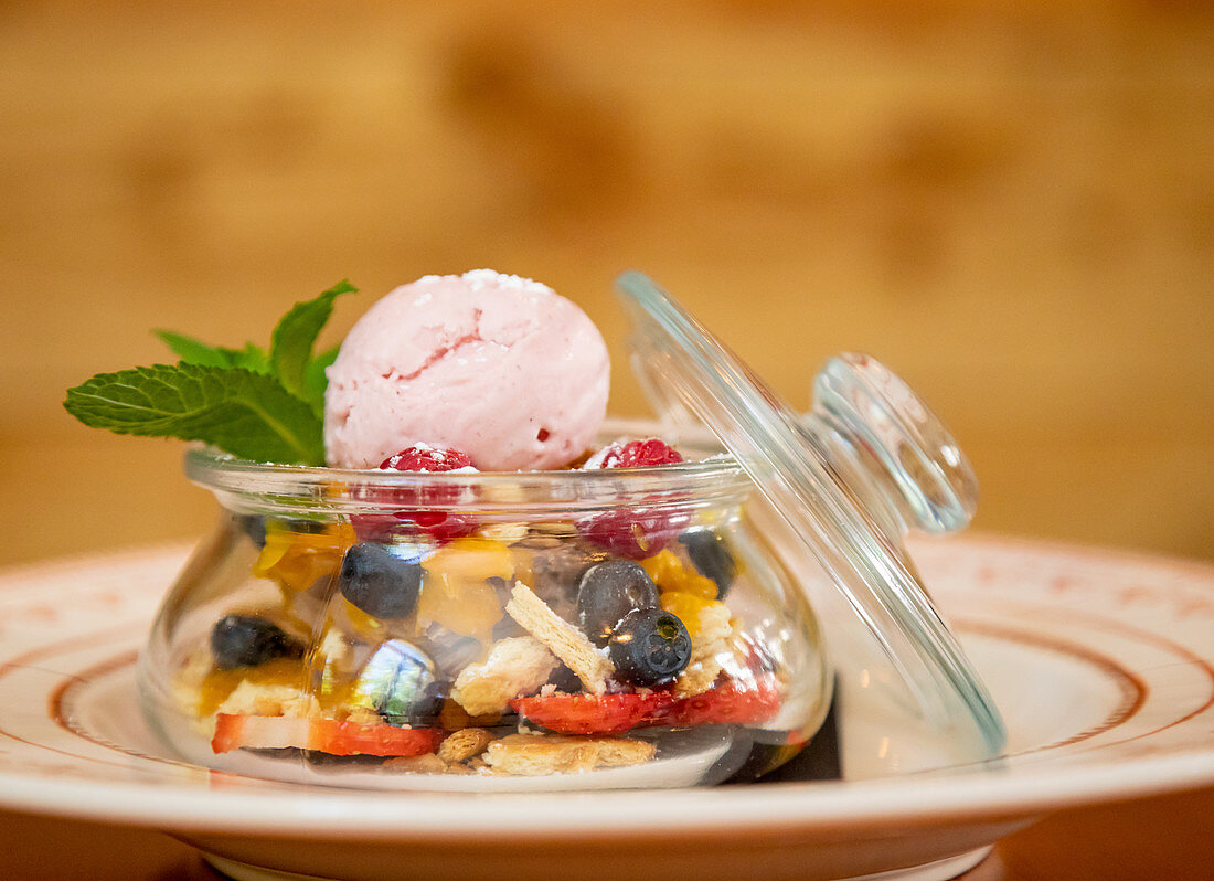 Scoop of ice cream in glass jar with various berries and garnished with sprig of mint