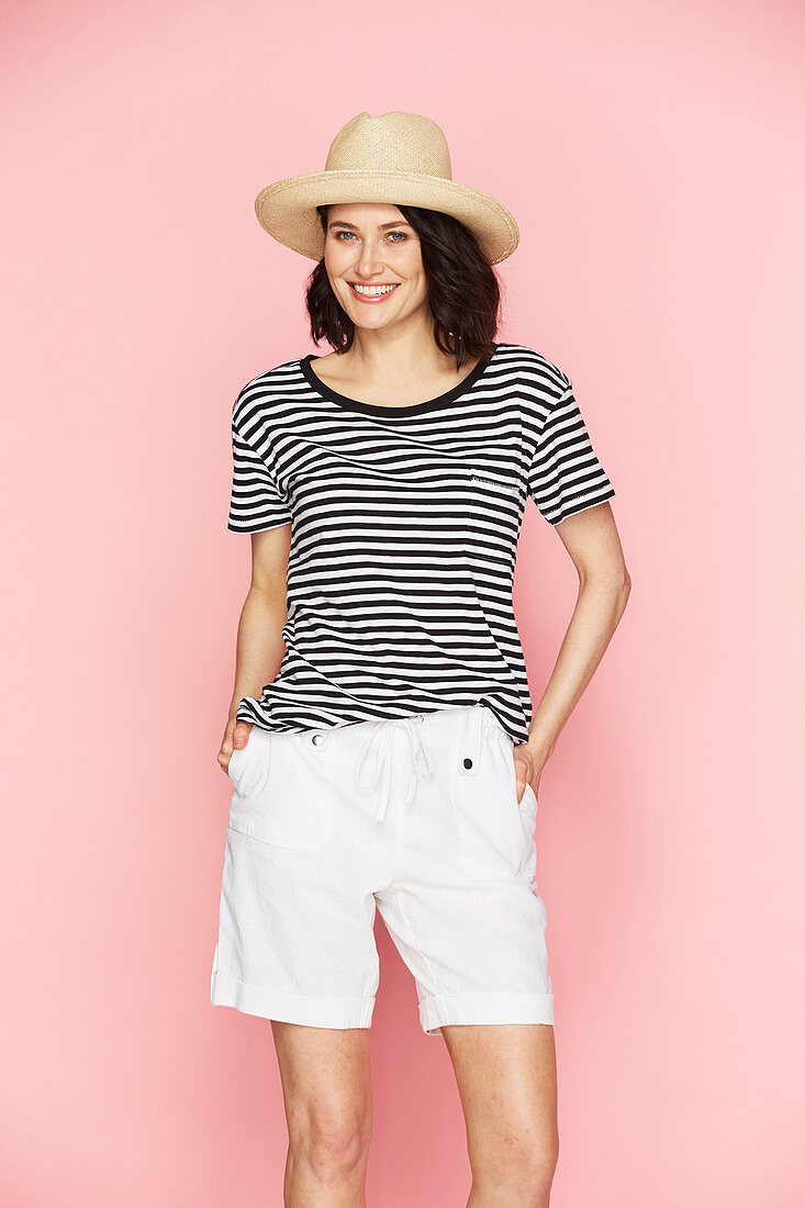 A brunette woman wearing a straw hat, a striped t-shirt and white shorts