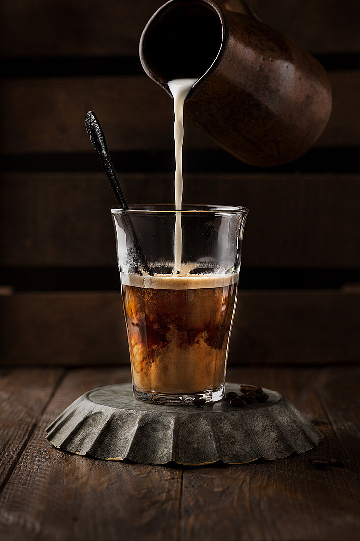 Frische Milch in Glas mit heißem Kaffee giessen