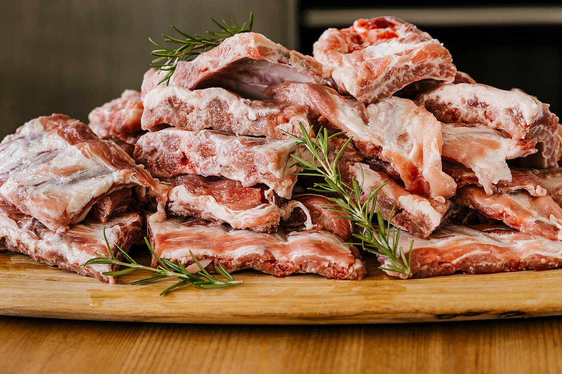 Heap of uncooked meat ribs with fat and aromatic rosemary sprigs