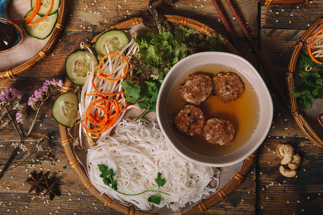 Bun Cha with meatballs and rice noodles served on plate with fresh herbs and vegetables