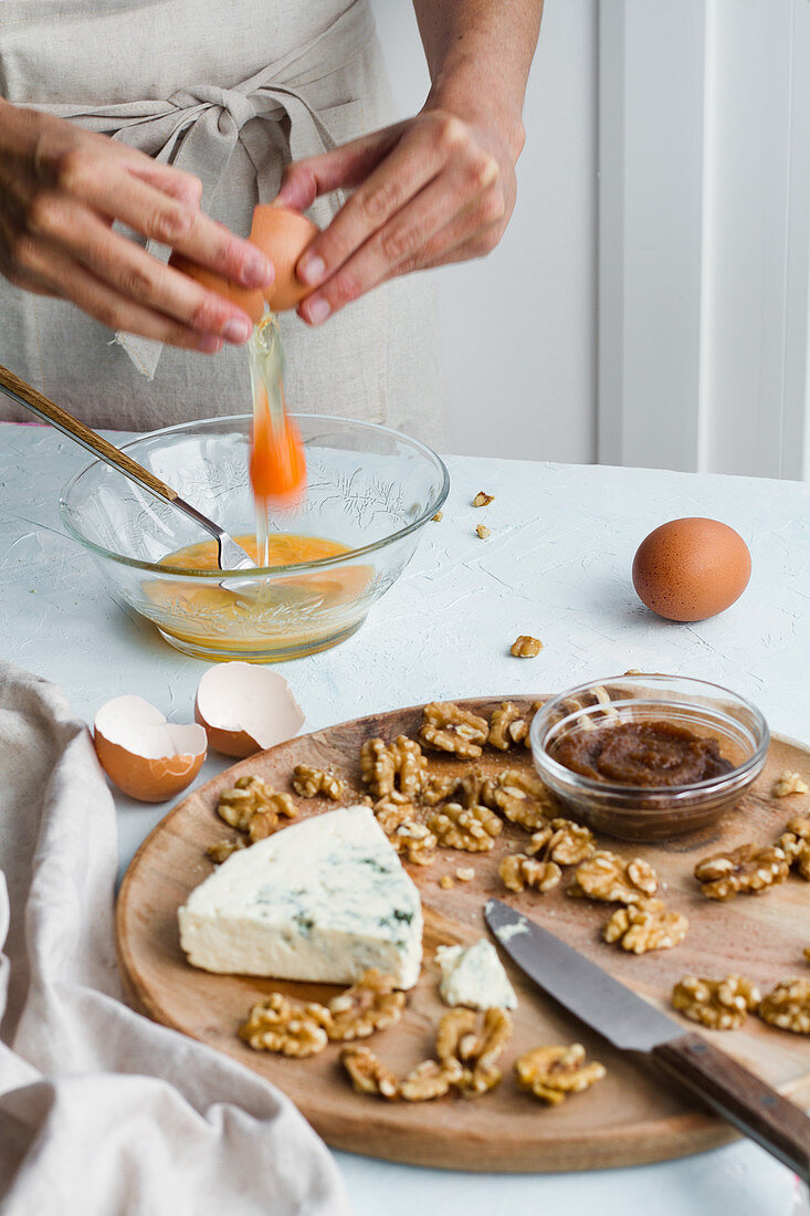 Adding eggs in glass bowl, walnuts and Blue cheesecake on wooden board
