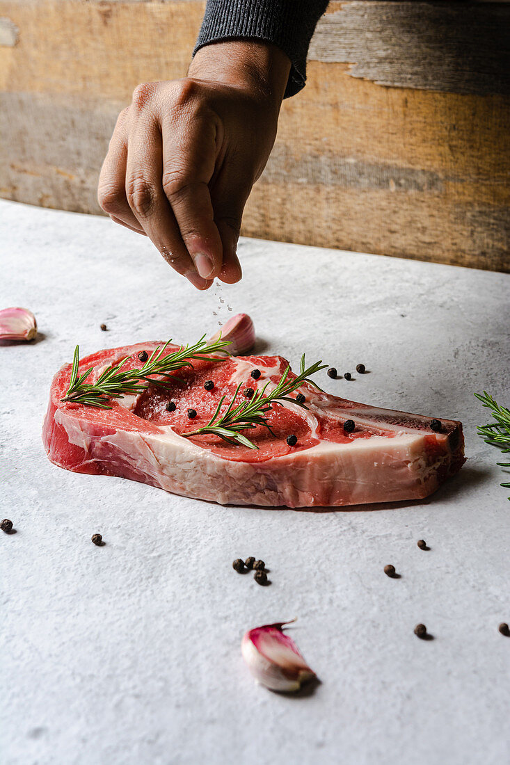 Sprinkling raw t bone beef steak with delicious condiment