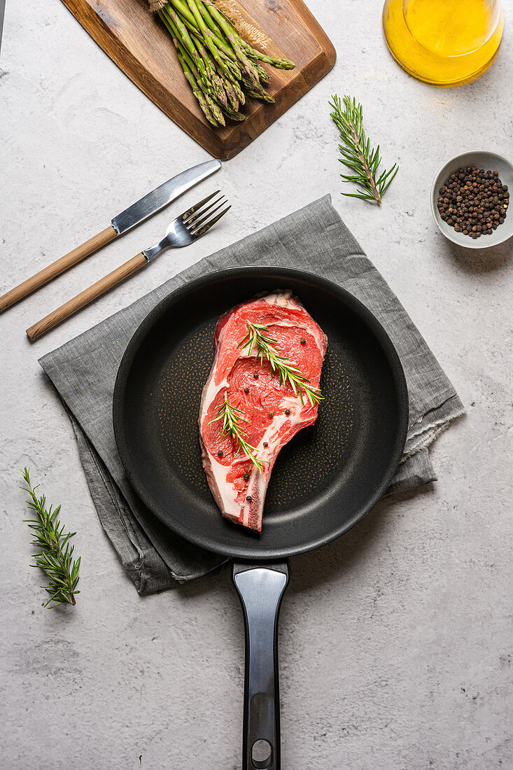 Raw t bone steak garnished with rosemary and black pepper in frying pan