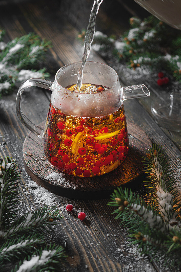 Brewing black tea with viburnum berries and lemon with fir branches and snow