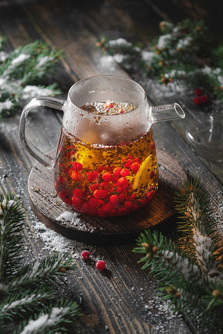 Brewing black tea with viburnum berries and lemon with fir branches and snow