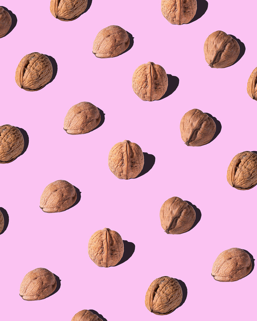 Walnuts arranged in rows on pink background