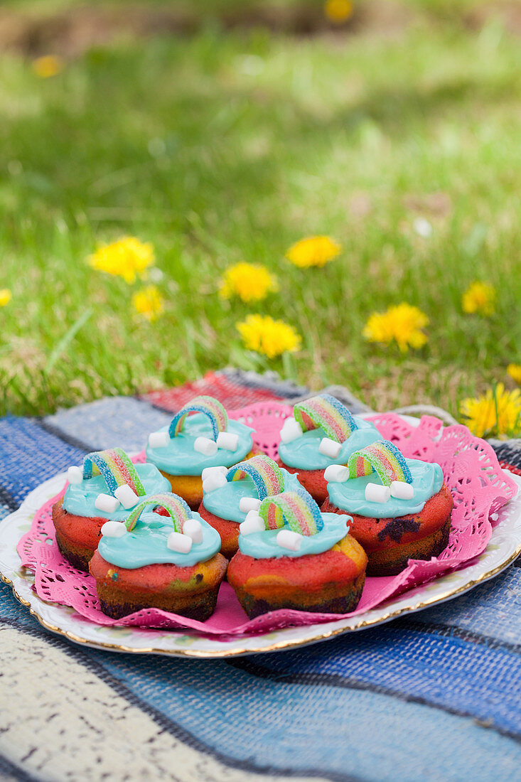 A plate of colorful muffins with rainbow decorations in a meadow