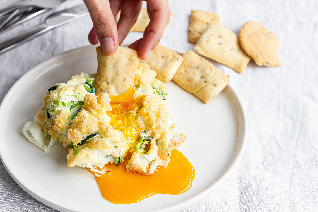 Hand dipping cracker in cloud eggs with green vegetables