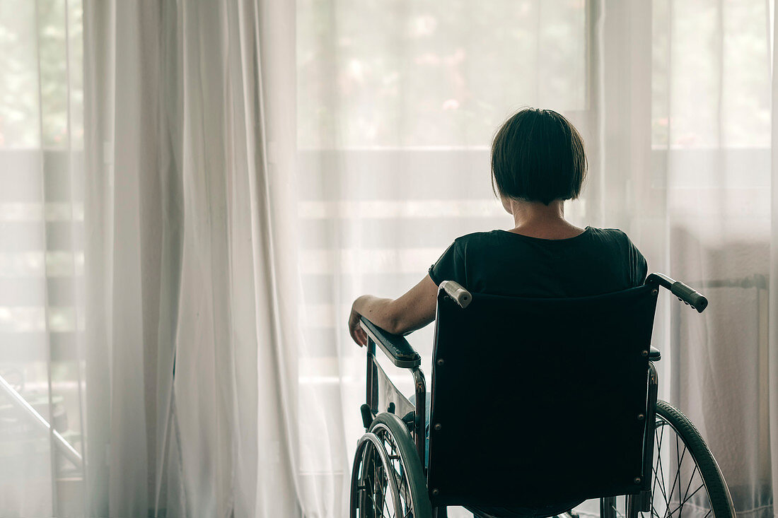 Depressed woman in wheelchair looking out the window