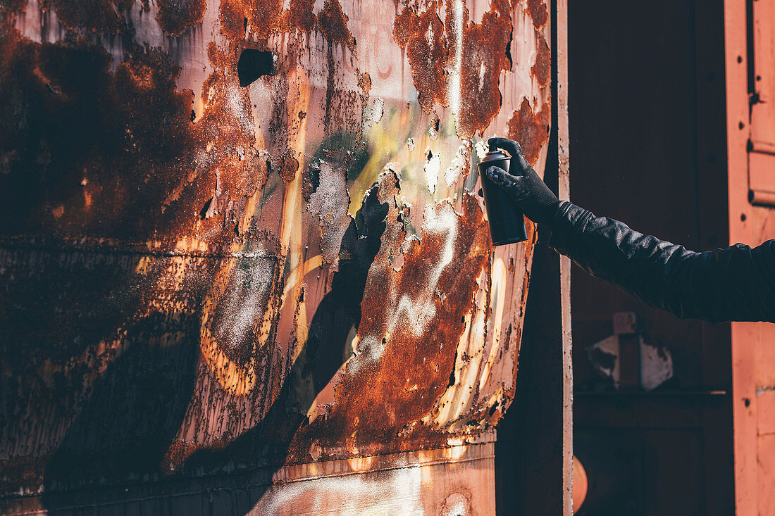 Man spray painting old train wagon with aerosol can