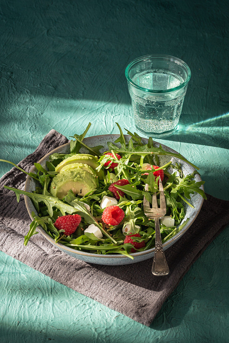 Salad with arugula and avocado garnished with cheese and fresh raspberries