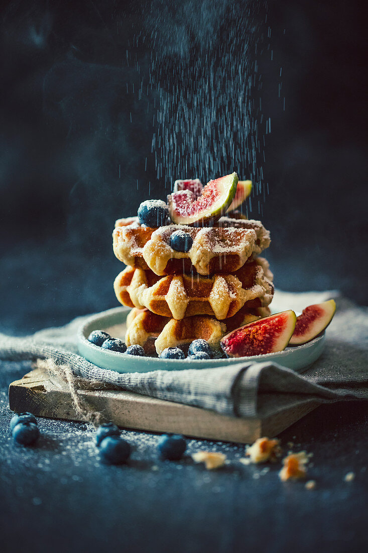 Puderzucker rieselt auf Marzipanwaffeln mit Amaretto, Blaubeeren und Feigen