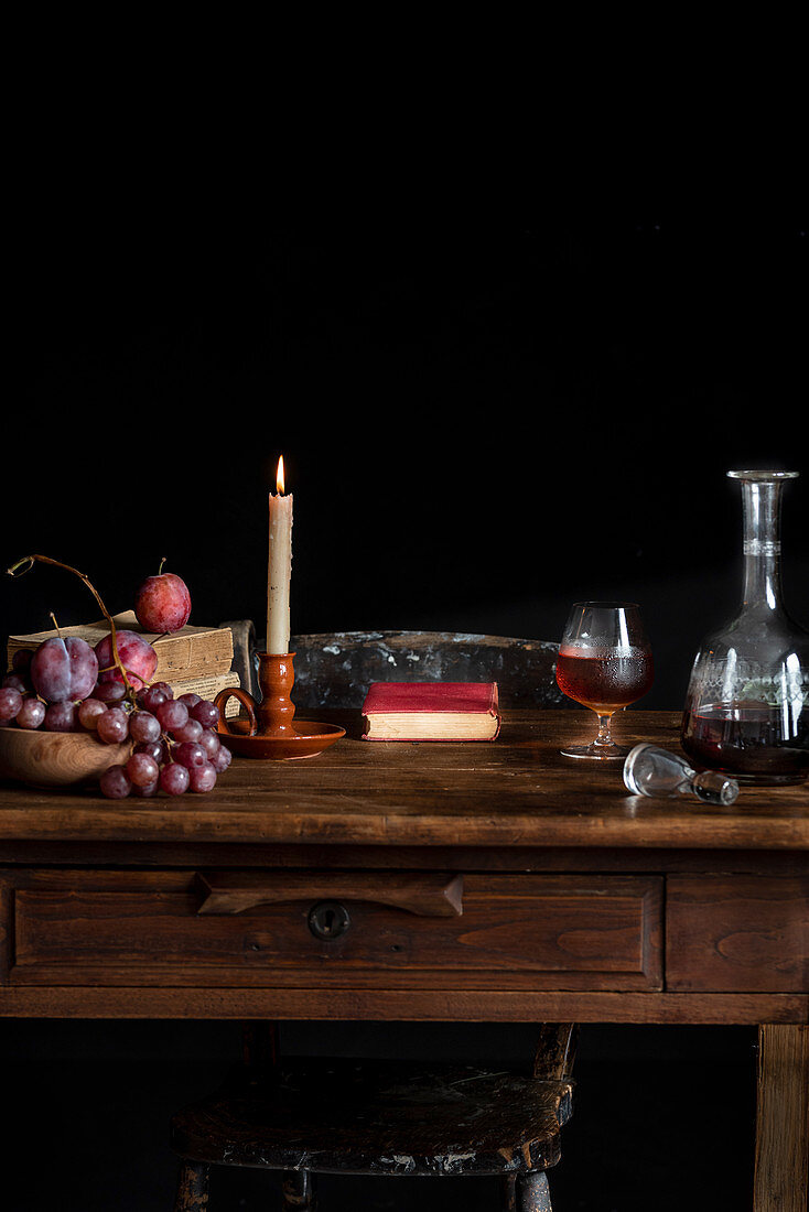 Holztisch mit Glas Cognac, Karaffe, Kerze und Trauben